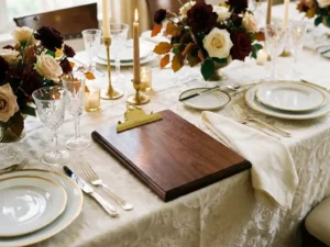 Evenementenplanner klembord op gedekte bankettafel met fijn porselein, kristallen glazen en seizoensgebonden bloemstukken bij kaarslicht.