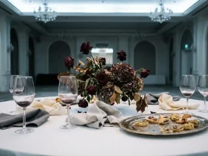 Verwelkt bloemstuk en halfvolle wijnglazen op een wit linnen banquettafel met verfrommelde servetten en onaangeroerde canapés.